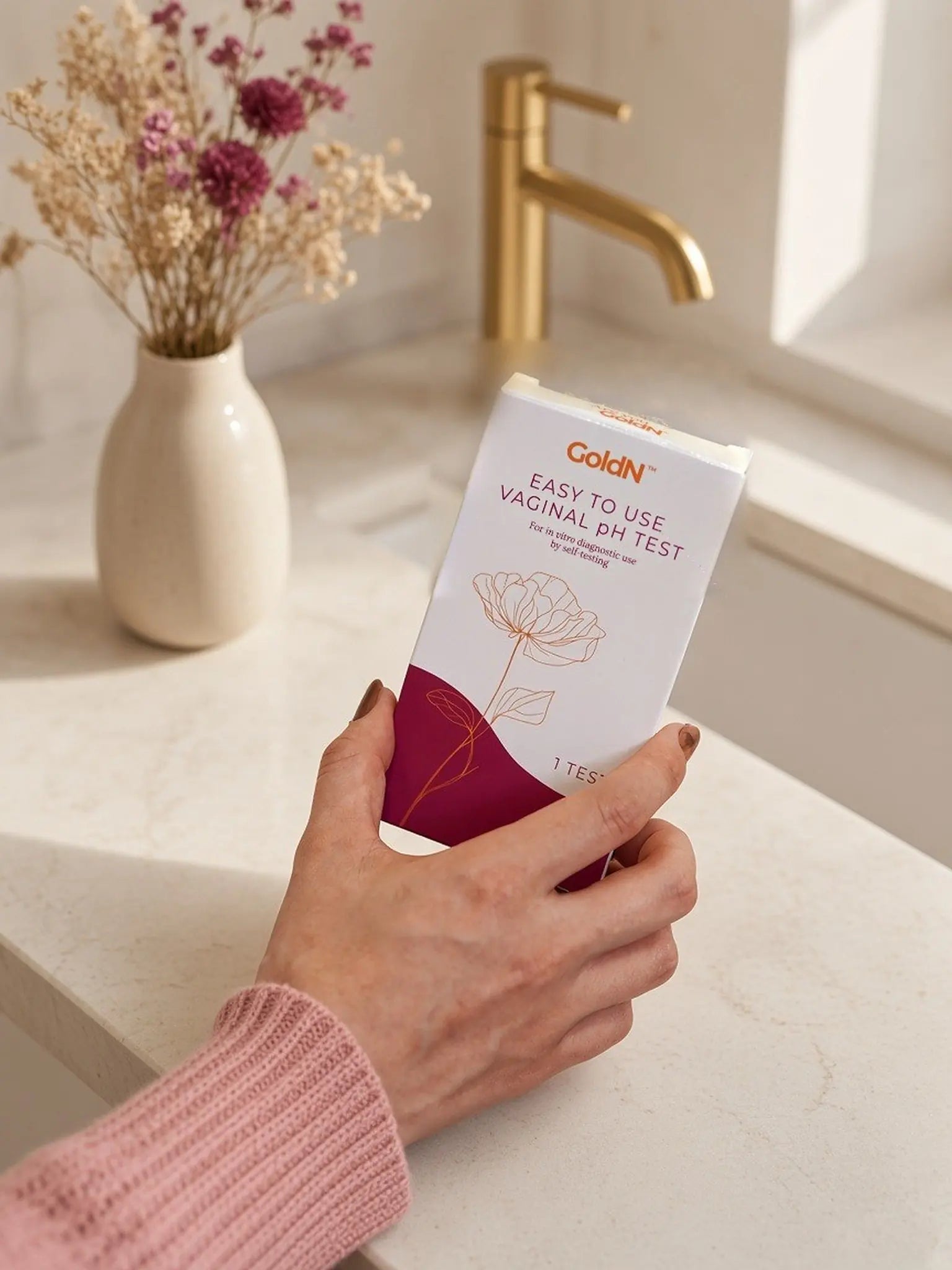 Hand holding the GoldN pH test box at a bathroom counter, label in focus