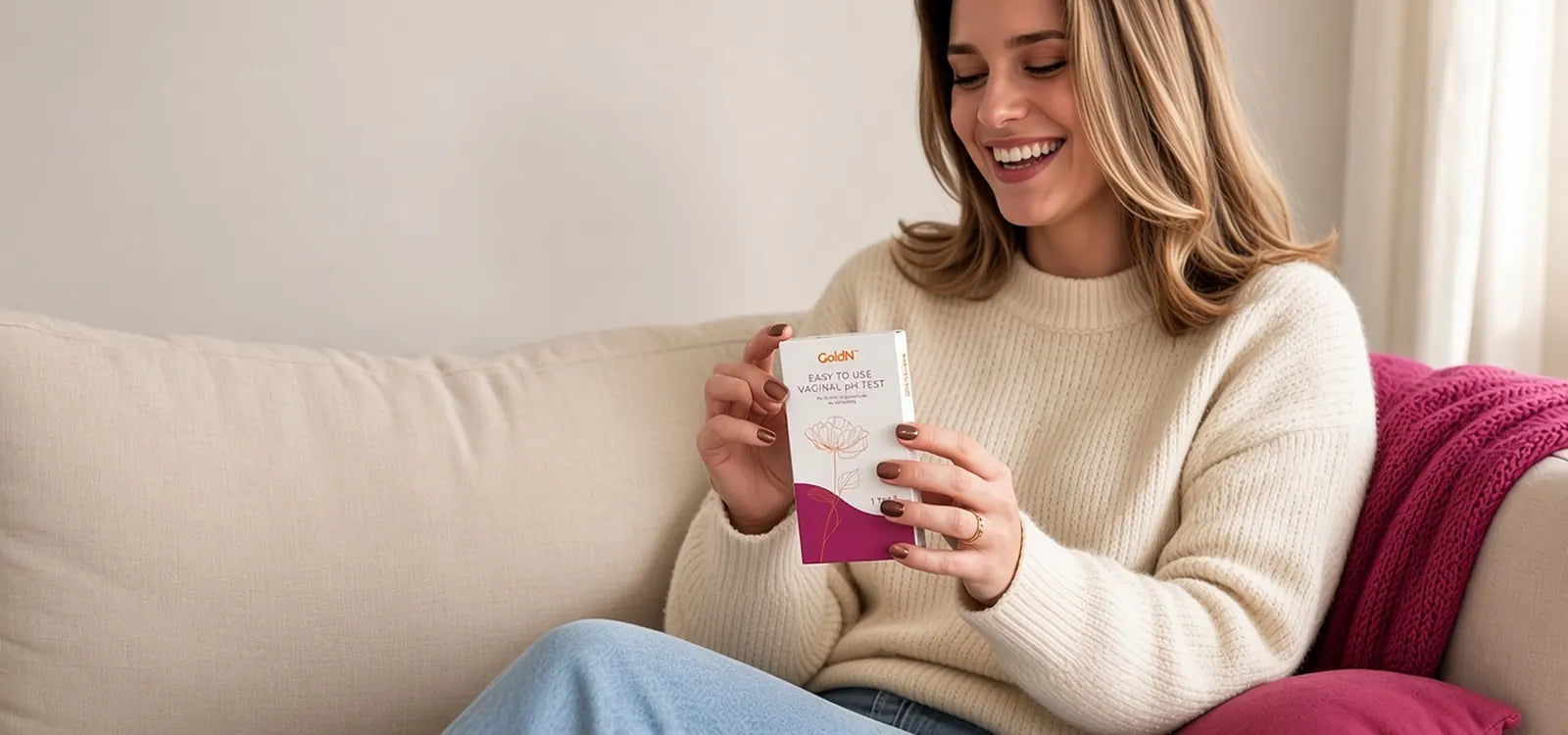 Woman on a cream sofa holding the GoldN Vaginal pH Test box