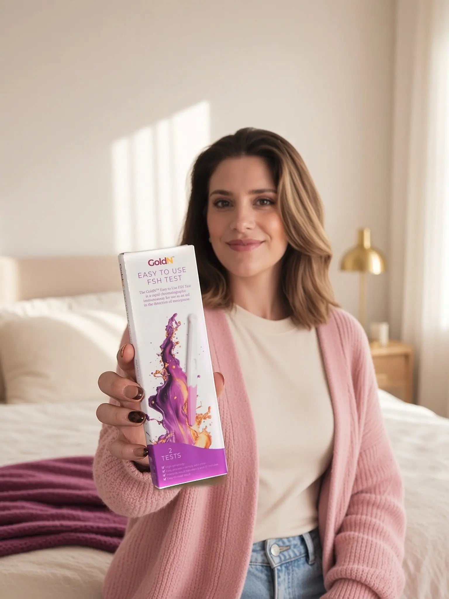 Woman in a bedroom holding the GoldN FSH test box toward the camera