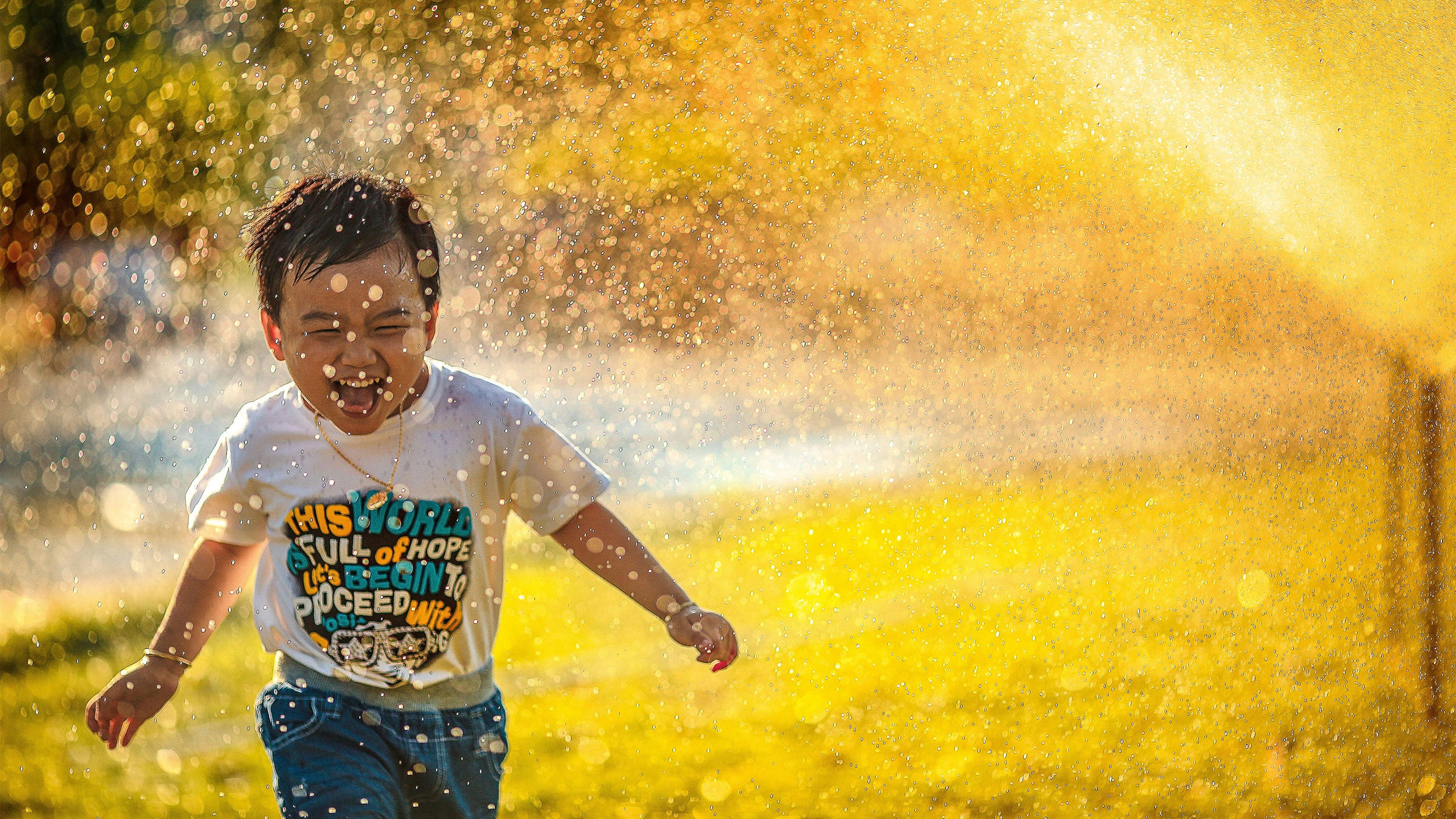 Happy boy running through yellow sprinklers