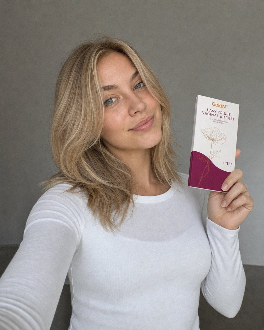 Woman in a white long-sleeve top holding the GoldN Vaginal pH Test box