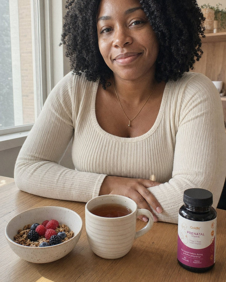 Woman at a breakfast table with tea, granola and the GoldN Prenatal bottle