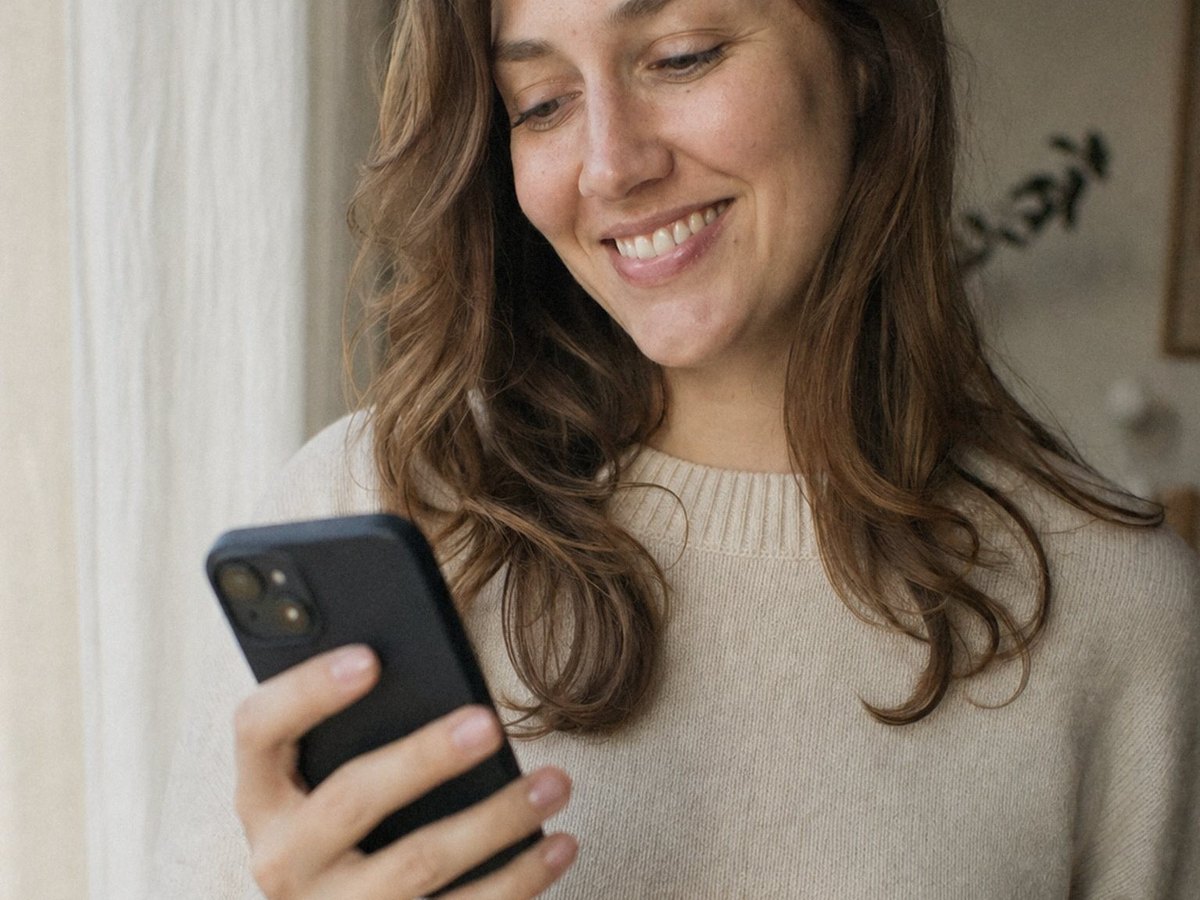 Woman smiling at her phone by a window