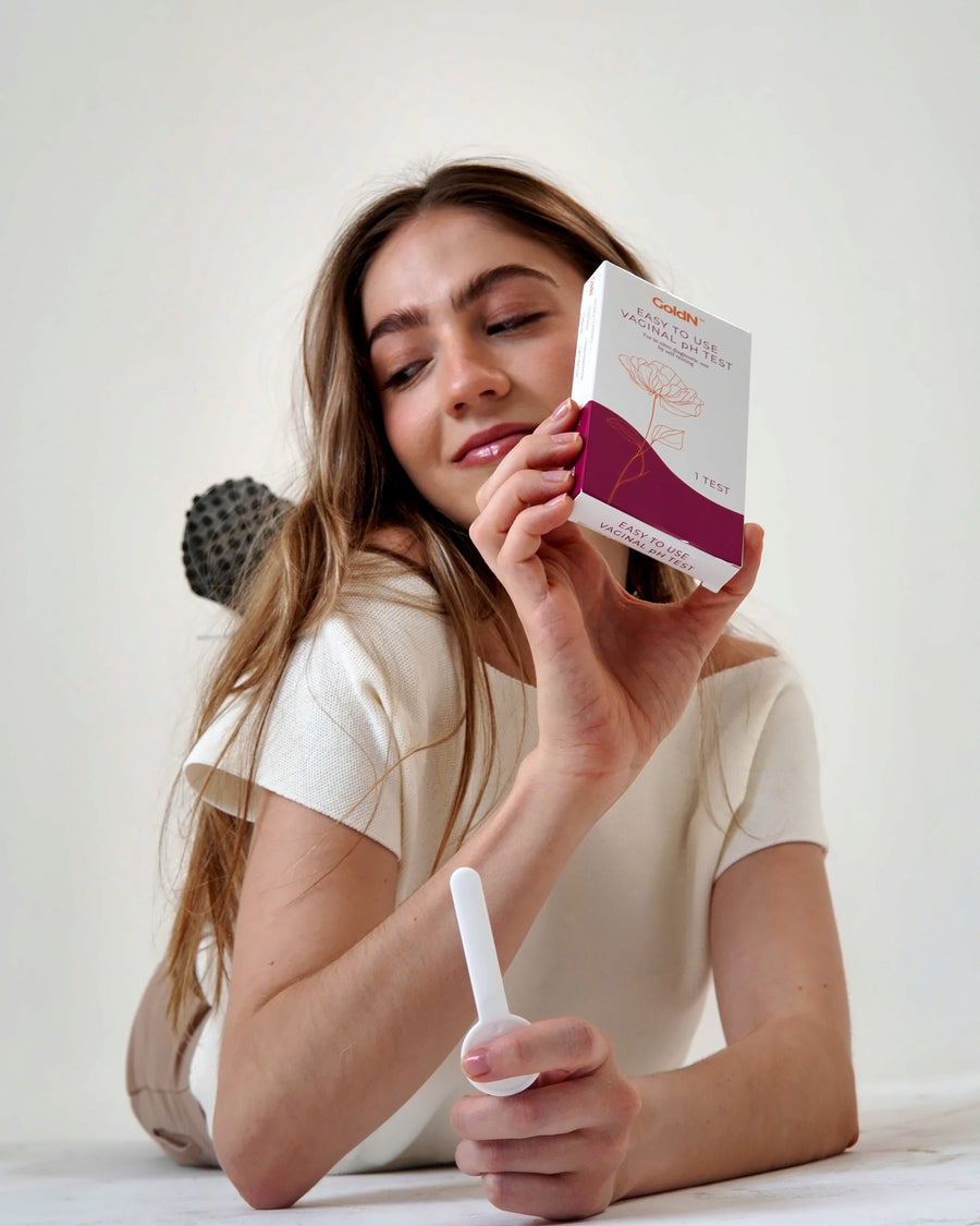 Woman holding the GoldN pH test box and swab next to her face in the studio