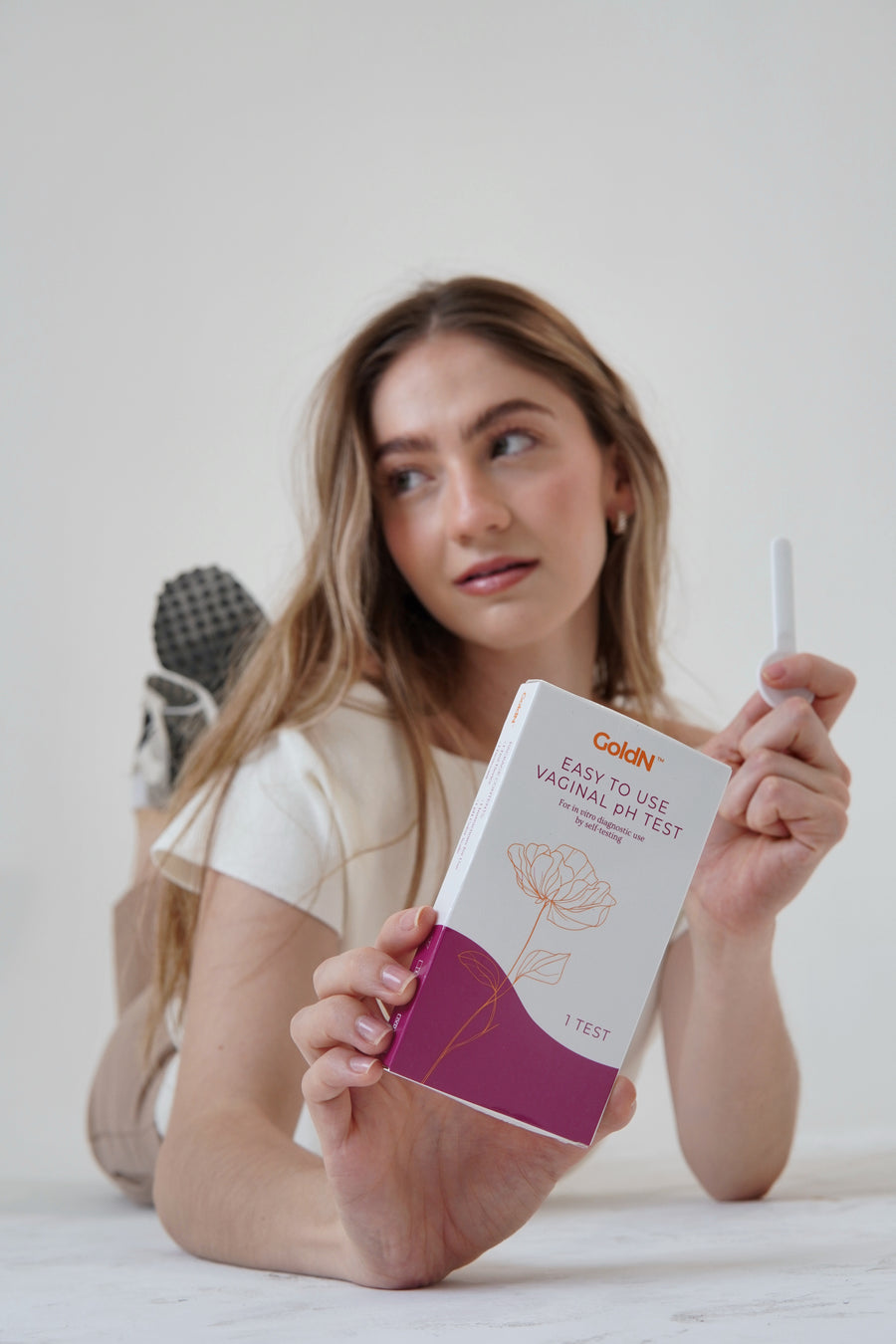 Woman holding the GoldN pH test box and swab toward the camera on a white background