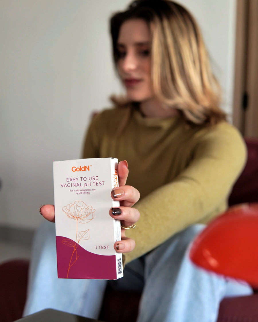 Hand holding the GoldN pH test box toward the camera on a sofa at home