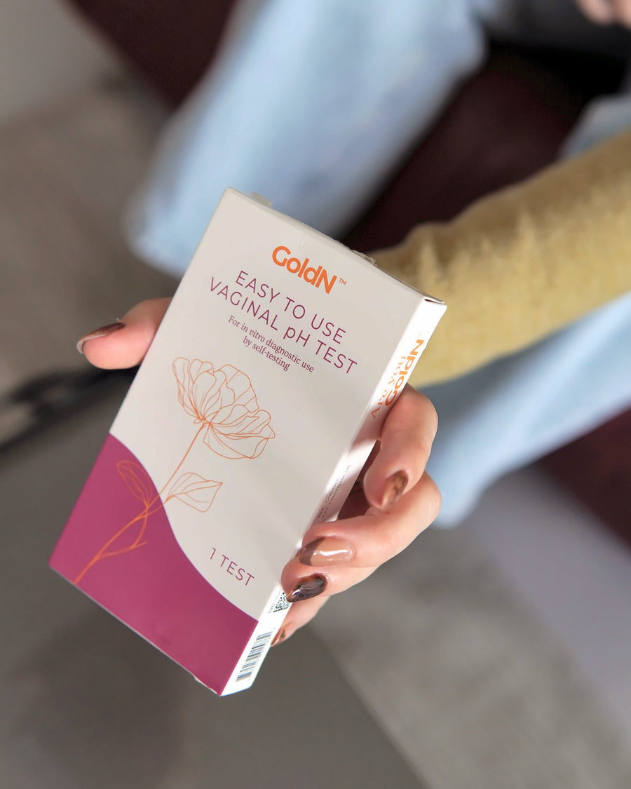 Hand holding the GoldN pH test box at home, label facing the camera