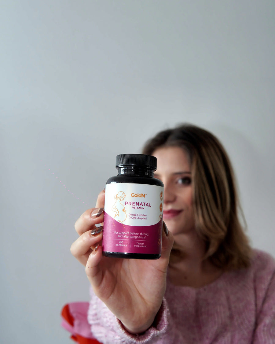 Hand holding the GoldN Prenatal with CoQ10 bottle toward the camera, label in focus