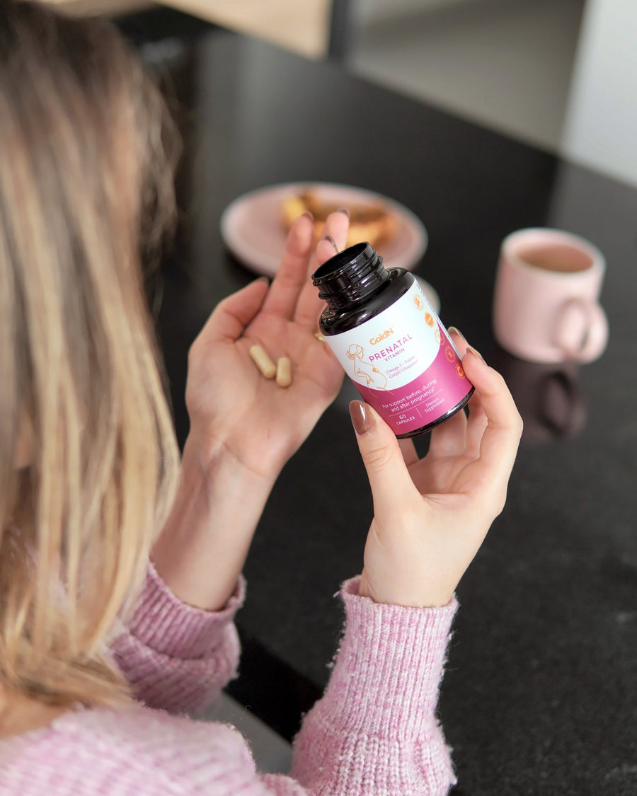 Capsules in a palm next to the GoldN Prenatal with CoQ10 bottle