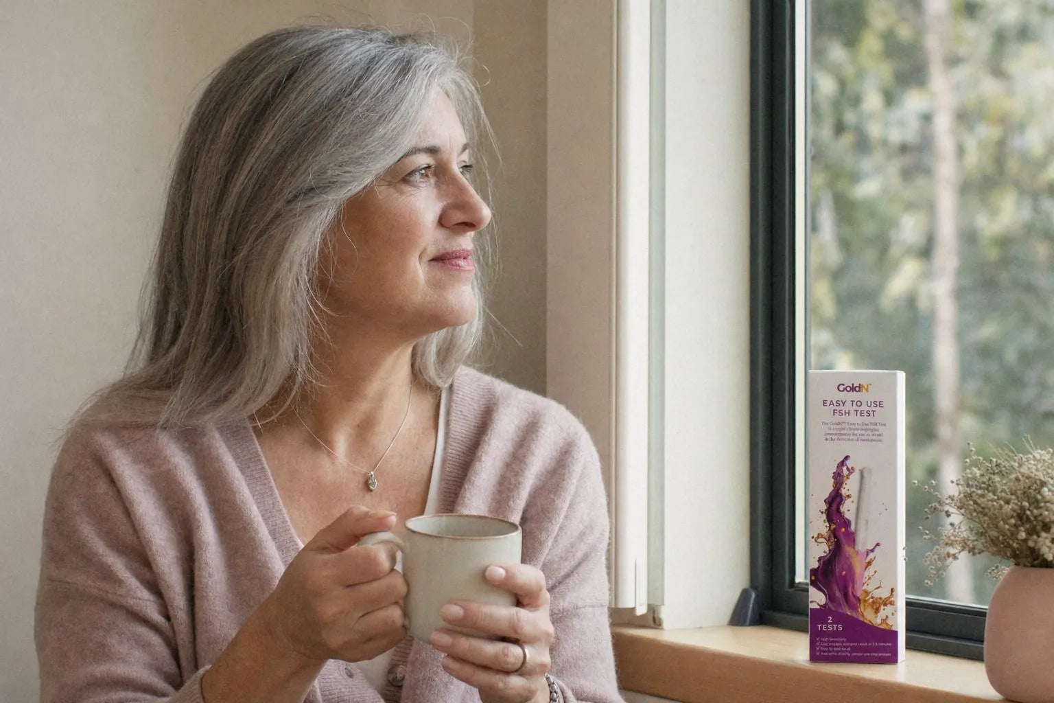 Woman with a cup of tea by a window, a GoldN FSH Test box on the sill